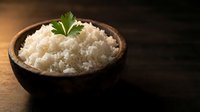 Cooked white rice in wooden bowl with fresh green herb garnish on dark wooden surface. Healthy grain staple food for Asian cuisine and meal preparation.