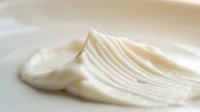 Creamy white cosmetic product with smooth texture spread on white surface, suitable for skincare, beauty, and wellness marketing materials.