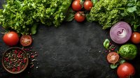 Fresh vegetables and spices frame on dark stone background with copy space, overhead view of cooking ingredients for healthy meal preparation.
