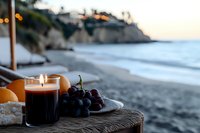Romantic beach setting with lit candle, fresh fruits and grapes on wicker table during sunset, coastal cliffs and ocean waves in background. Perfect for wellness.