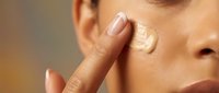 Young woman applying cream moisturizer to face with finger, skincare routine beauty treatment for healthy glowing skin and anti-aging care.
