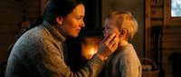 Loving father gently holding young son's face in cozy firelit living room, showing tender parental care and family bonding moment in warm home setting.
