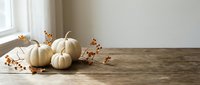 White pumpkins and autumn berries arranged on rustic wooden table by window creating cozy fall seasonal decoration for home interior design projects.