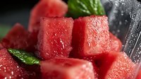 Fresh juicy watermelon cubes with water drops and green mint leaves on dark background, macro shot showing texture and natural sweetness for food design.