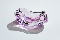 Curved pink glass bowl with organic flowing shape casting soft shadow on white surface. Elegant transparent crystal decorative object with modern design.