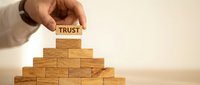 Hand placing wooden block with trust text on pyramid of blocks representing business foundation and reliability concepts for corporate presentations.