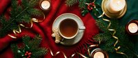 Festive Christmas tea cup with holiday decorations, pine branches, red ribbon, golden ornaments and candles on dark background for seasonal greeting cards.