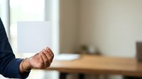 Businessman holding blank white paper sheet in office environment with wooden desk and window light.