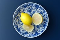 Fresh yellow lemon whole and sliced on blue and white floral ceramic plate, top view on dark blue background, food styling concept.