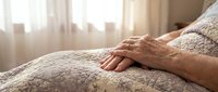 Elderly hands resting peacefully on soft knitted blanket in warm sunlit bedroom creating serene atmosphere of comfort and relaxation at home.