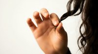 Close-up of a hand grasping long dark hair against a neutral background, depicting concepts of stress, tension, frustration, or emotional distress for healthcare and wellness content.