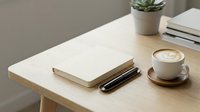 Young professional workspace with open notebook, pen, coffee cup, succulent plant and books on wooden desk for business and productivity concepts.