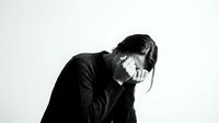 Young Asian man in dark sweater experiencing headache or stress, holding head in hands against white background for mental health concepts.