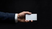 Professional businessman hand holding blank white business card against dark background for corporate branding and marketing materials.