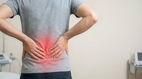 Man experiencing lower back pain holding spine with hands showing red inflammation area in medical office setting for healthcare concepts.