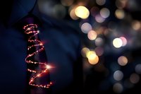 Glowing spiral Christmas tree made of warm LED lights against dark blue background with colorful bokeh lights creating festive holiday atmosphere.