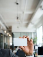 Businessman holding blank white business card in modern office environment with blurred background, suitable for corporate branding and professional networking materials.