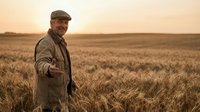 Smiling senior Caucasian male farmer extending hand for handshake in golden wheat field at sunset, warm harvest season atmosphere.