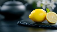 Fresh yellow lemons on dark slate board with water drops, citrus fruits for cooking and healthy nutrition concepts in modern kitchen setting.