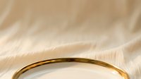 Close-up of elegant gold ring resting on soft beige fabric with natural lighting, suitable for jewelry marketing and luxury product photography.