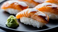 Fresh salmon nigiri sushi with wasabi on black plate, close up view showing tender raw fish slices layered over seasoned rice, traditional Japanese cuisine.