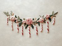 Festive embroidered garland with pink flowers and candy canes on neutral fabric background, perfect for holiday decoration and crafting projects.