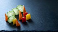 Fresh cucumber slices with colorful bell pepper pieces arranged on dark slate surface for healthy cooking and meal preparation concepts.