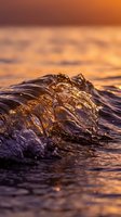 Ocean wave crashing with golden sunset light reflecting on water surface creating dramatic seascape with warm orange and purple sky colors.