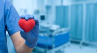 Healthcare worker in blue gloves holding red heart symbol in hospital setting representing medical care, cardiology and compassionate patient treatment.