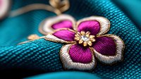 Vibrant pink and gold embroidered flower on turquoise fabric with intricate stitching details and metallic thread accents, showcasing delicate needlework craftsmanship.