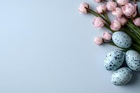Speckled blue quail eggs with delicate pink spring tulips arranged on light blue background, creating soft seasonal composition for Easter and spring designs.