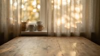 Empty wooden table surface with blurred window background and warm sunlight streaming through curtains for product display and montage purposes.
