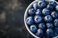 Fresh ripe blueberries in white bowl on dark wooden background. Healthy organic superfood berries for breakfast, smoothies and desserts.