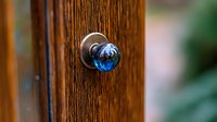 Vintage blue glass doorknob on wooden door creates nostalgic atmosphere. Crystal sphere reflects light with deep azure tones against rich brown wood grain texture.