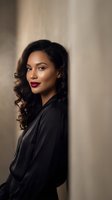Professional African American businesswoman with curly hair and red lipstick in black blazer posing confidently against neutral background for corporate headshot.