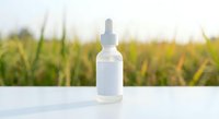 White dropper bottle with pipette on clean surface against blurred natural green field background for skincare serum cosmetic product mockup.