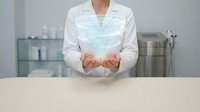 Female healthcare professional in white lab coat presenting holographic medical data visualization with cupped hands in modern clinical laboratory setting.