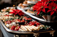 Festive holiday catering spread featuring gourmet appetizers, charcuterie, and fresh ingredients arranged on elegant platters with vibrant red poinsettia flowers for seasonal events and celebrations.