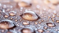 Macro photography of water droplets on metallic surface creating abstract pattern with copper and silver tones. Artistic close-up shows surface tension and light reflection.
