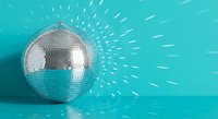 Shiny disco ball reflecting light rays on turquoise background creating sparkle effect for party and nightclub entertainment events.