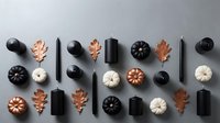 Autumn flat lay with black candles, copper and white pumpkins, oak leaves arranged on gray background for seasonal home decor and holiday styling.