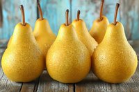 Fresh ripe yellow pears arranged on rustic wooden table with soft blue background for healthy eating and organic fruit concepts.