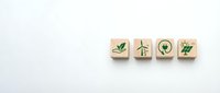 Four wooden blocks with green eco-friendly icons including leaf, wind turbine, light bulb and plant on white background for sustainable business concepts.
