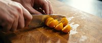 Person with knife slicing golden yellow bell pepper on wooden cutting board with flour dusting, food preparation for cooking and culinary use.