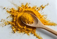 Vibrant turmeric powder scattered on white surface with wooden spoon, highlighting golden yellow spice used in cooking and natural medicine.