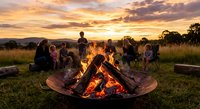 Group of diverse friends gathering around campfire at sunset sharing stories and enjoying outdoor adventure together in natural countryside setting.