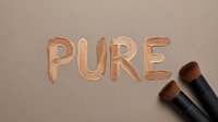 Liquid foundation makeup in warm nude tone with the word pure spelled out, accompanied by professional cosmetic brushes on neutral background.