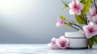 Cosmetic cream jar with delicate pink spring flowers and green leaves on white wooden surface against soft gray background for spa and beauty.