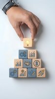 Hand placing lightbulb block on pyramid of wooden cubes with business icons representing innovation, growth, and success concepts for corporate strategy.
