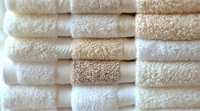 Neatly stacked fresh cotton towels in cream and white shades create luxurious spa atmosphere, close up view showing soft terry cloth texture and layers.